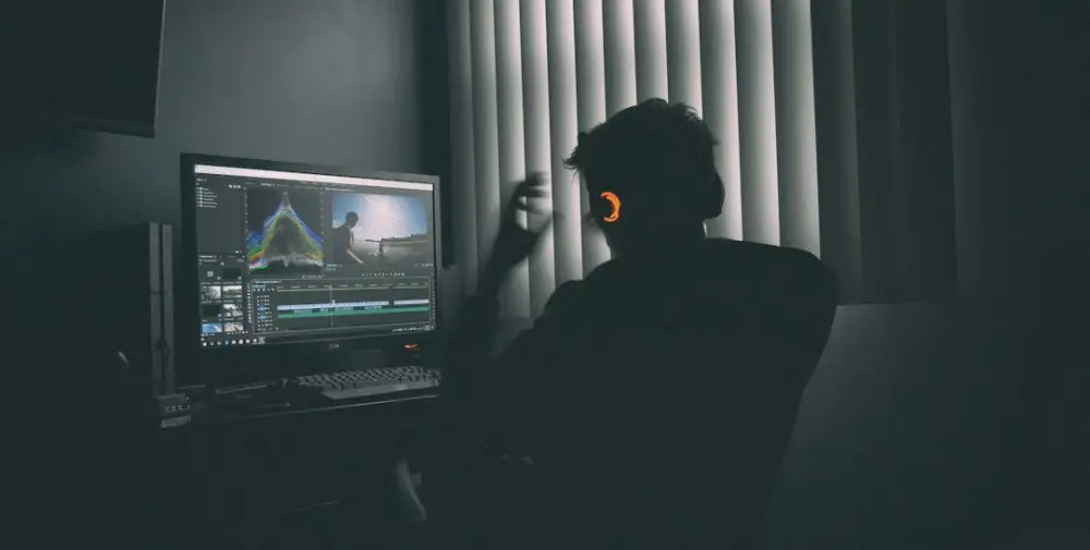 A person in silhouette wearing headphones editing video on a computer in a dark room, illustrating maintaining narrative